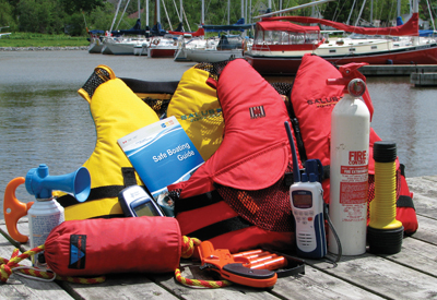 A selection of winter-ready safety equipment—life jackets, an EPIRB, and cold-weather gear—spread out on the deck, surrounded by the golden leaves of a nearby tree. The image emphasizes preparedness for colder conditions, enhancing the blog’s focus on essential safety gear for off-season voyages.<br />
